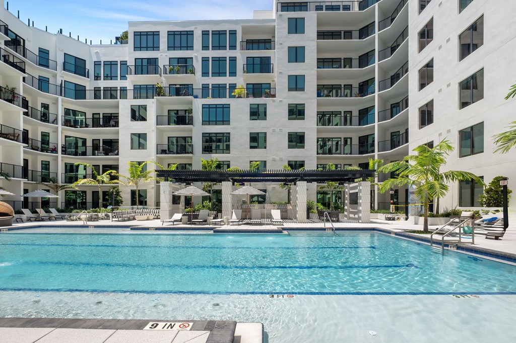 A large swimming pool in front of a white building with balconies.