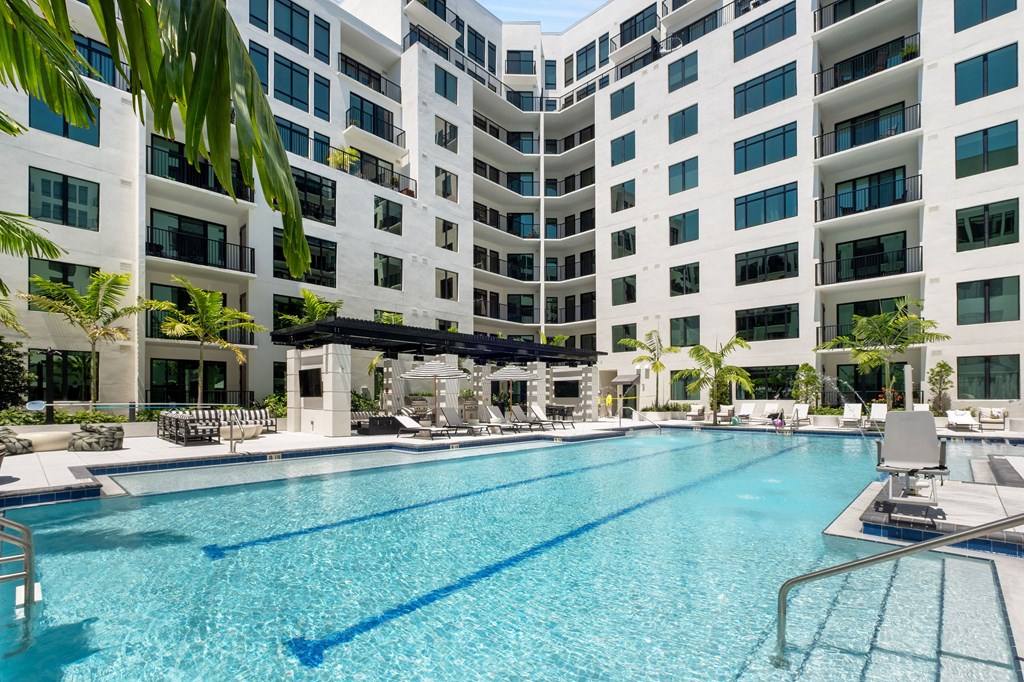 A large swimming pool in front of a white building with palm trees.