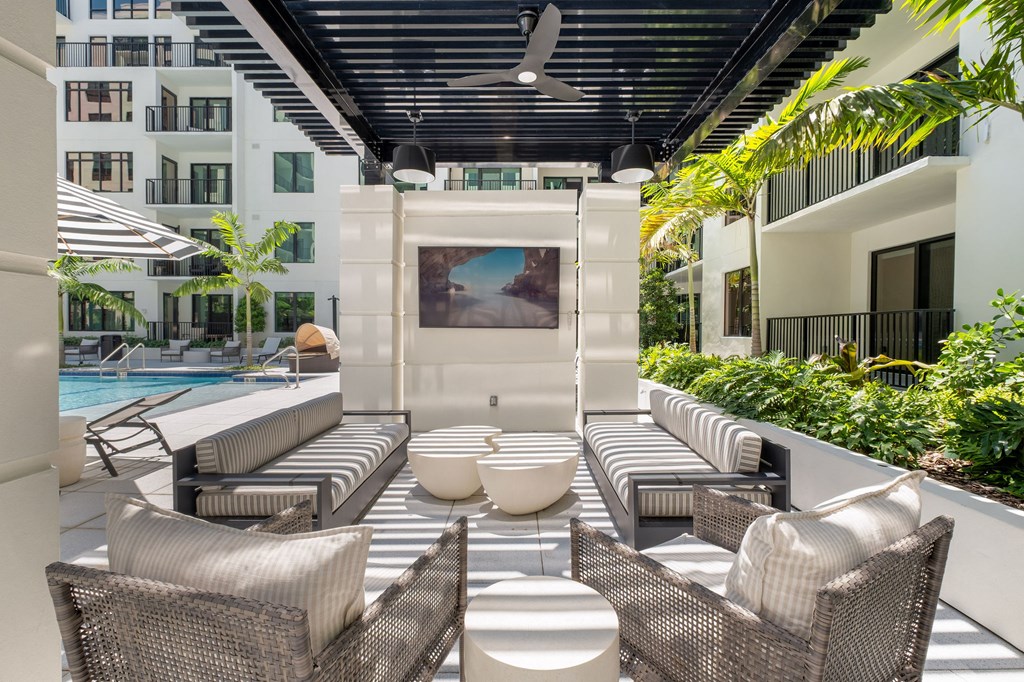 A patio with a white couch and chairs with a pool in the background.