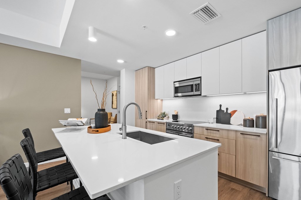 A modern kitchen with a white countertop and black chairs.