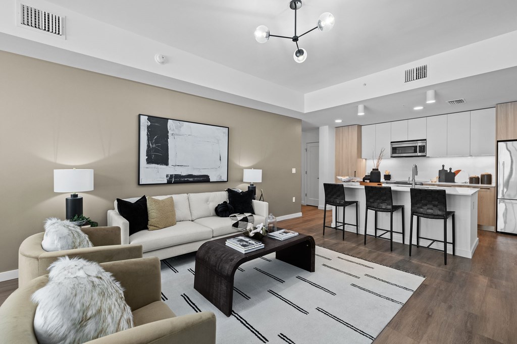 A modern living room with a white couch, a coffee table, and a kitchen area in the background.