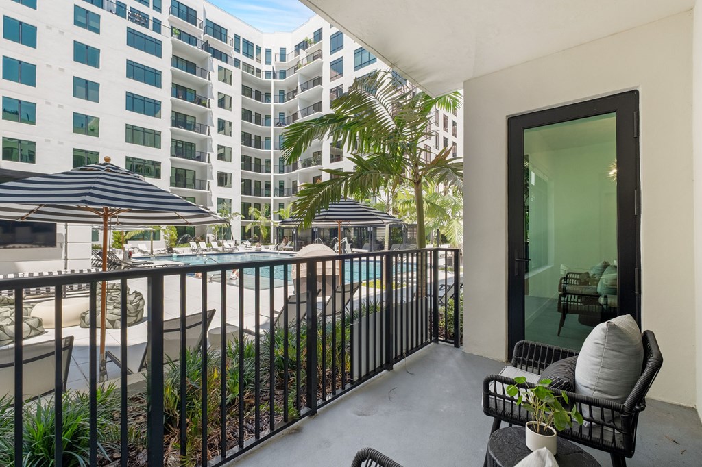 A balcony with a table and chairs overlooking a pool and buildings.