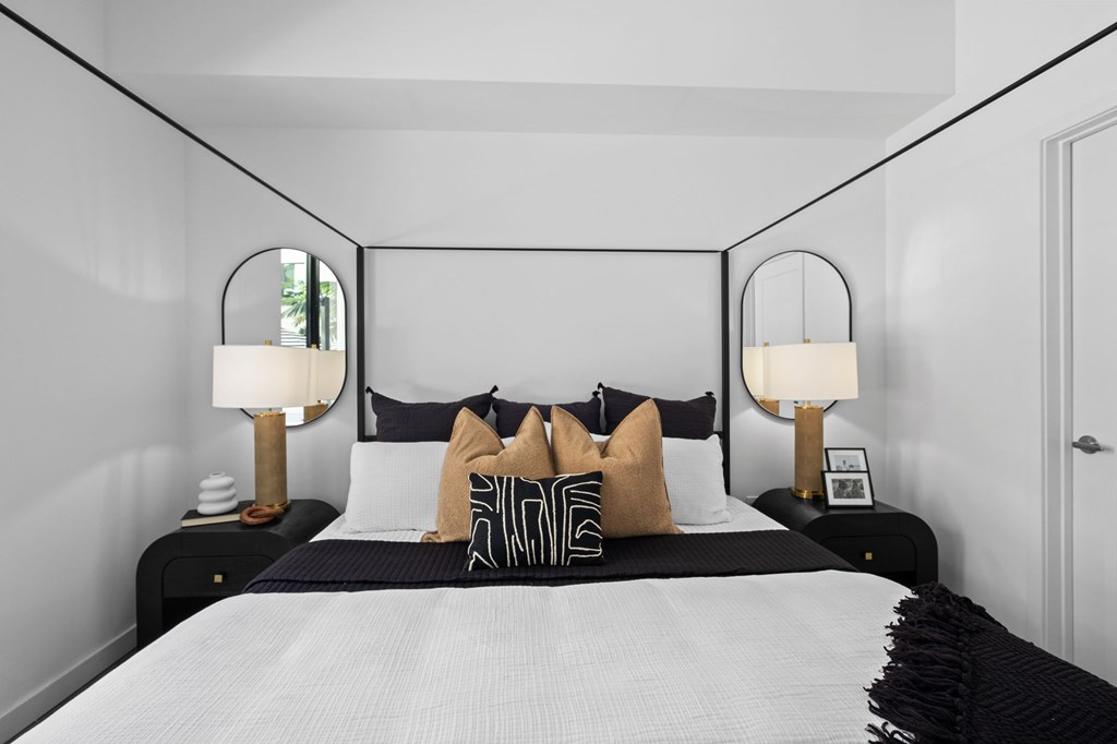A bed with a white comforter and a black headboard with two lamps on each side.