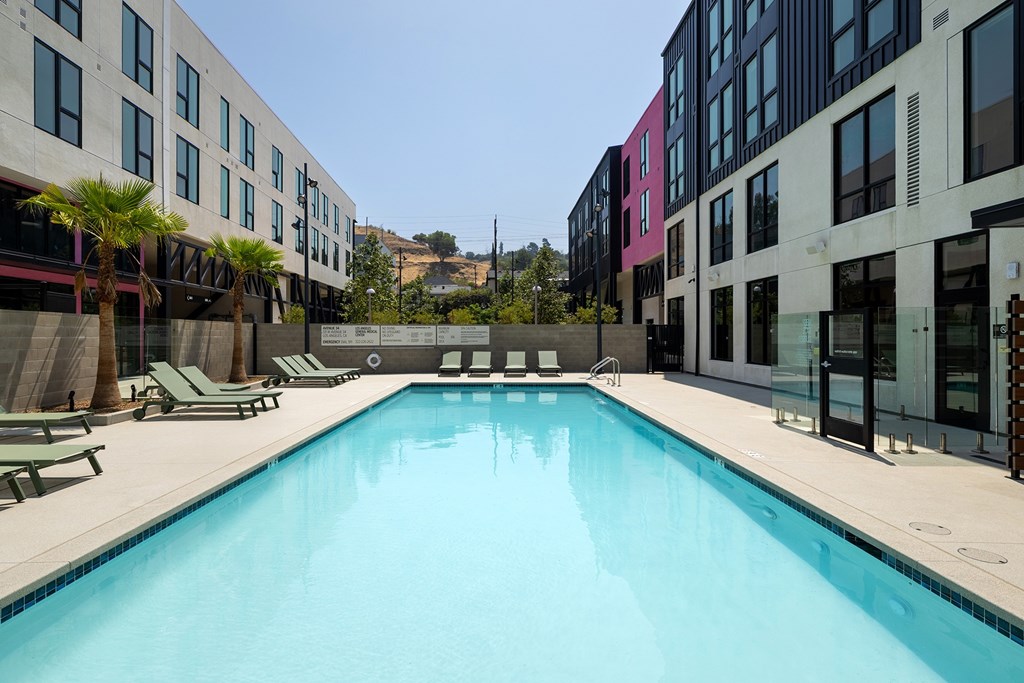A gated swimming pool with lounge chairs and palm trees.