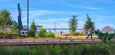 a woman walking on a train track with a view of the bay bridge