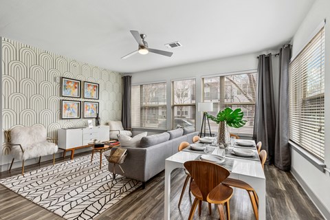 A modern living room with a grey couch, a white dining table, and a patterned rug.