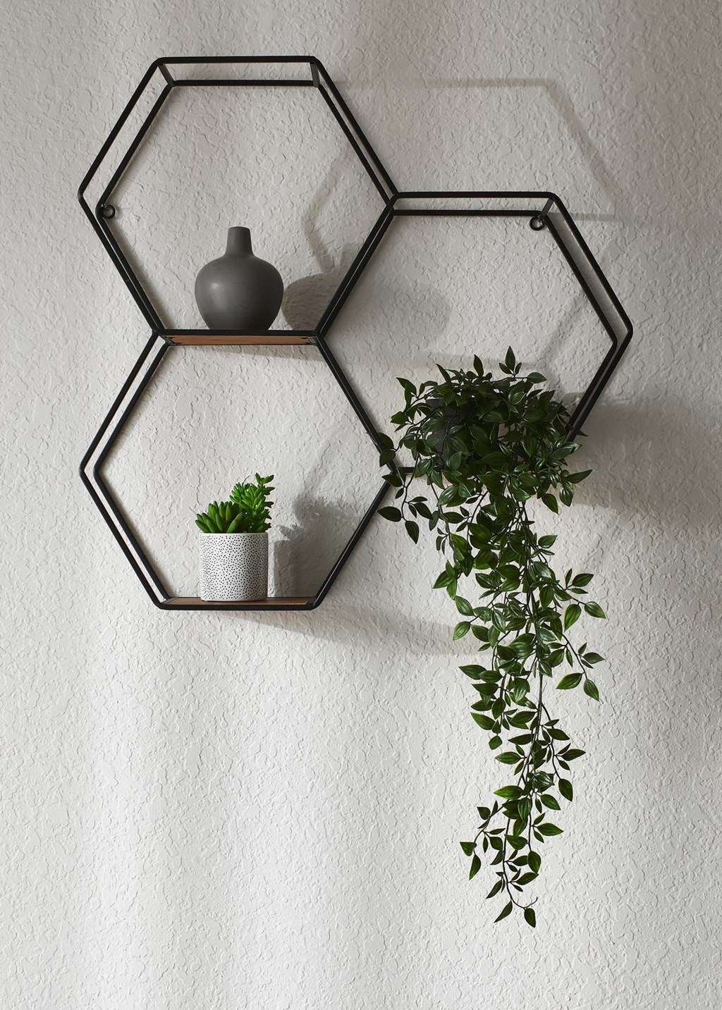 a metal hexagon shelf with a vase and a plant hanging on a wall