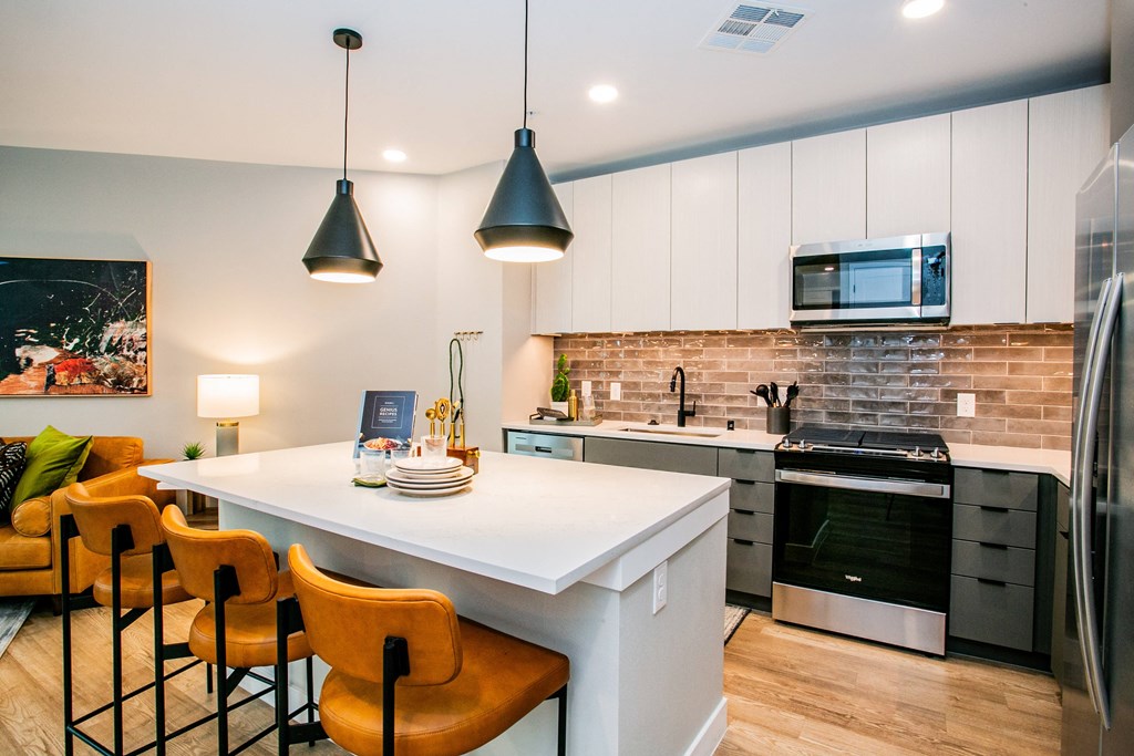 a kitchen with white cabinets and a large white island with a white countertop and orange chairs