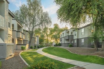 A row of modern apartment buildings with a well-maintained lawn and trees in the foreground.