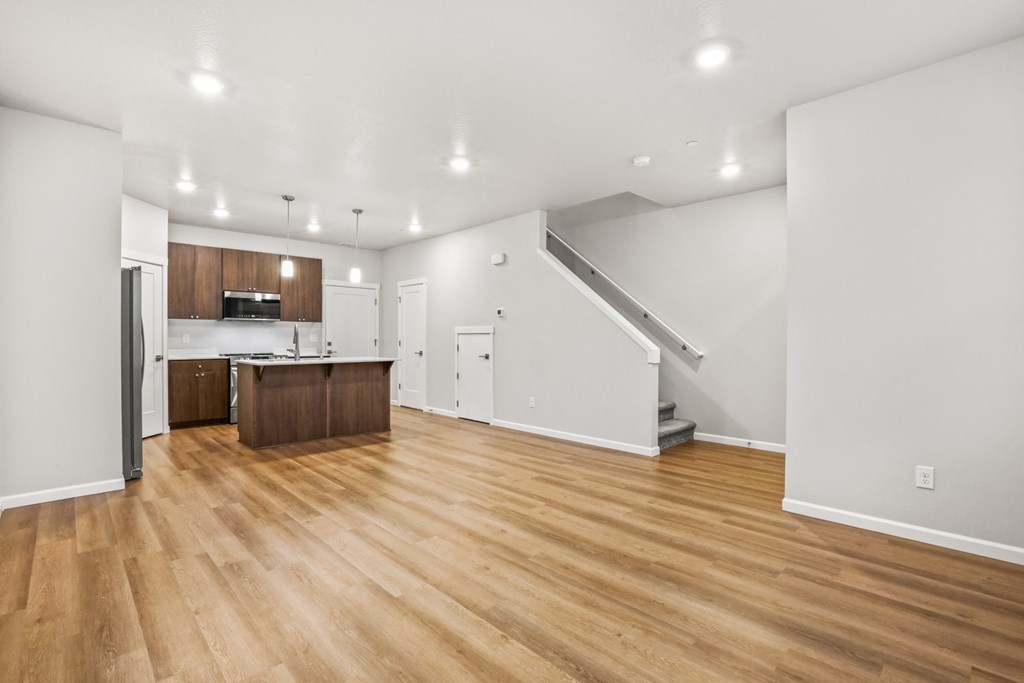 the living room and kitchen of a house with white walls and wood floors