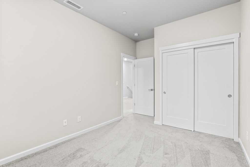 an empty bedroom with white doors and a carpeted floor