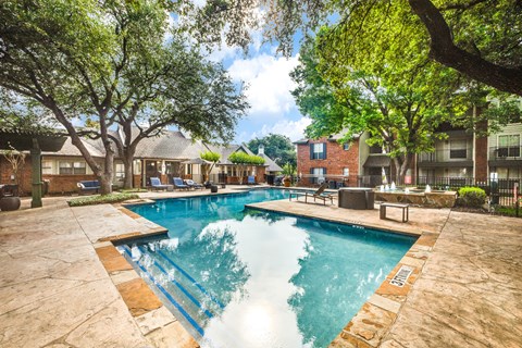 A swimming pool surrounded by trees and a building in the background.