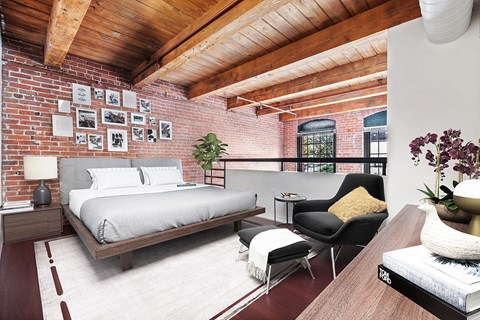 loft bedroom with exposed brick and wood beam ceilings over looking the large living room with a ton of natural light.