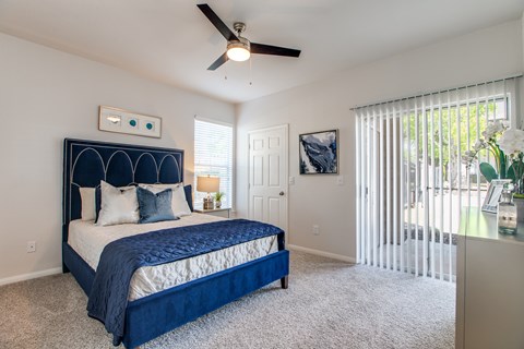 A bedroom with a blue bedspread and a ceiling fan.