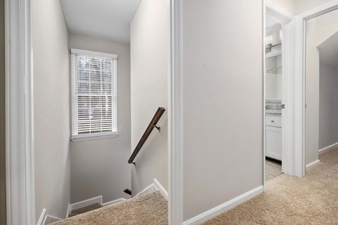 A hallway with a carpeted floor and a staircase leading to the second floor.