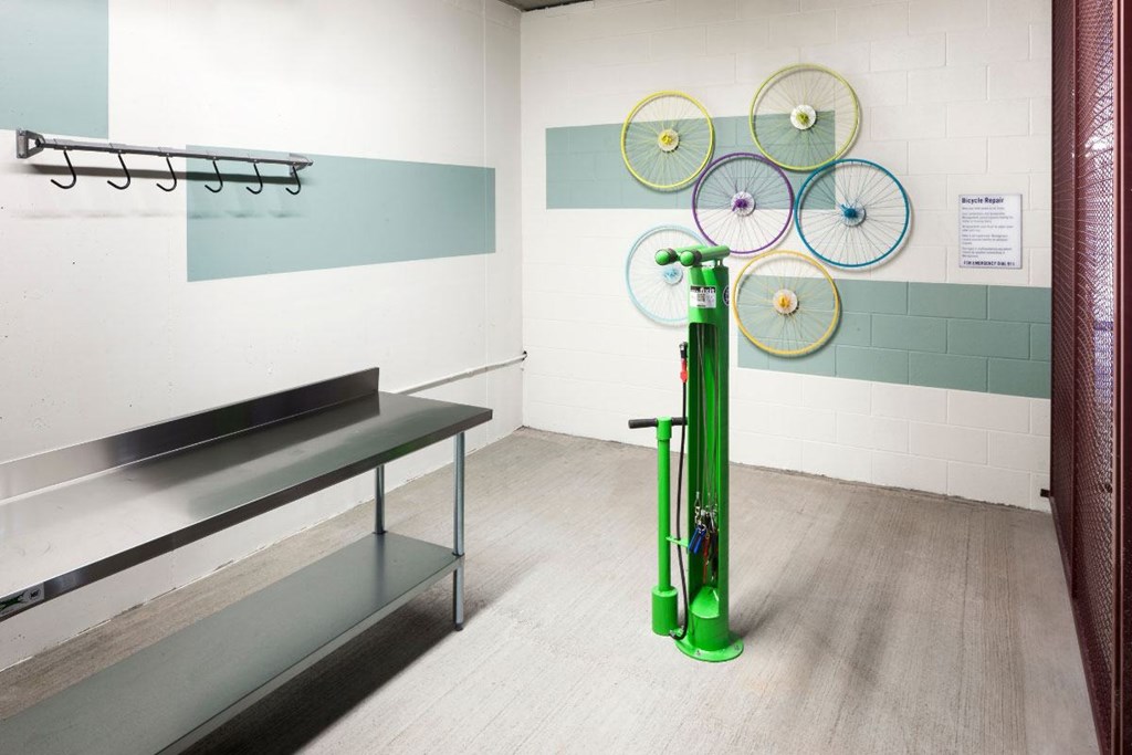 A green vacuum cleaner stands in a room with a wall hanging of bicycle wheels.