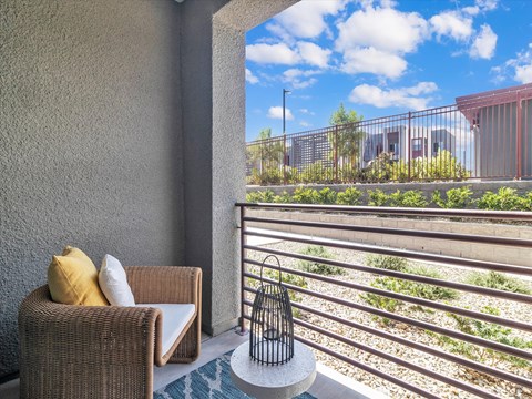 A balcony with a wicker chair and a table with a birdcage on it.