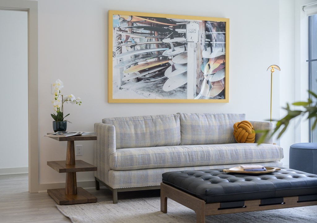 A grey couch with a yellow pillow sits in front of a framed picture.