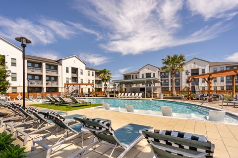 A pool area with sun loungers and a building in the background.