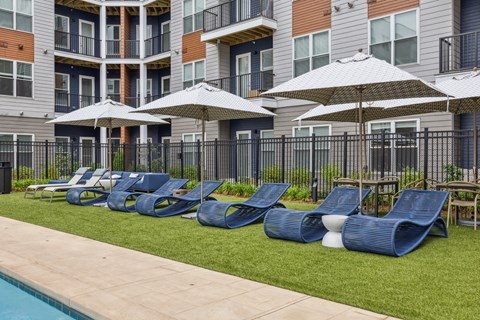 a row of lounge chairs and umbrellas in front of an apartment building