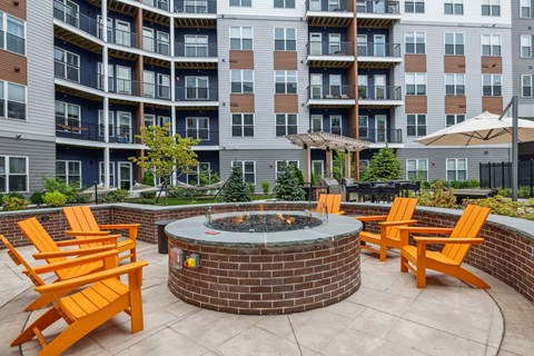 an outdoor patio with a fire pit and chairs in front of an apartment building