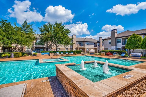 A large swimming pool with a fountain in the middle surrounded by a brick wall.