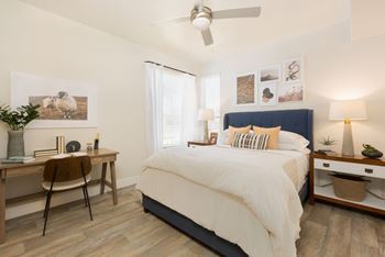A bedroom with a bed, desk, chair, and a ceiling fan.