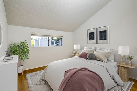 A bedroom with a bed, two lamps, and a potted plant.