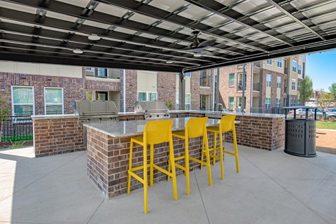 a patio with a bar with yellow chairs and a grill