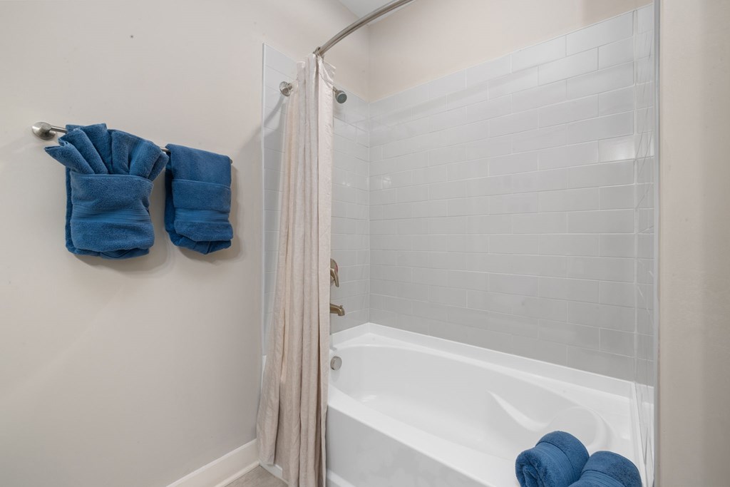 A white bathtub with a shower curtain and towels hanging on the wall.