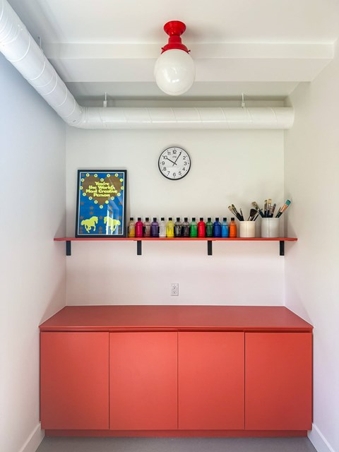 A red cabinet sits under a clock on a white wall.