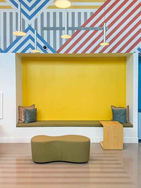 A yellow wall with a bench and a green ottoman in front of it.