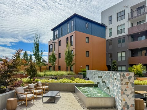 A modern outdoor seating area with a water feature in front of a multi-story building.