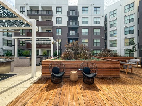 A wooden deck with two chairs and a table in the foreground with apartment buildings in the background.