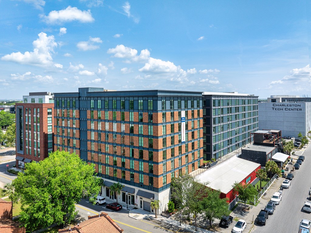 A large building with a glass facade is surrounded by trees and other buildings.