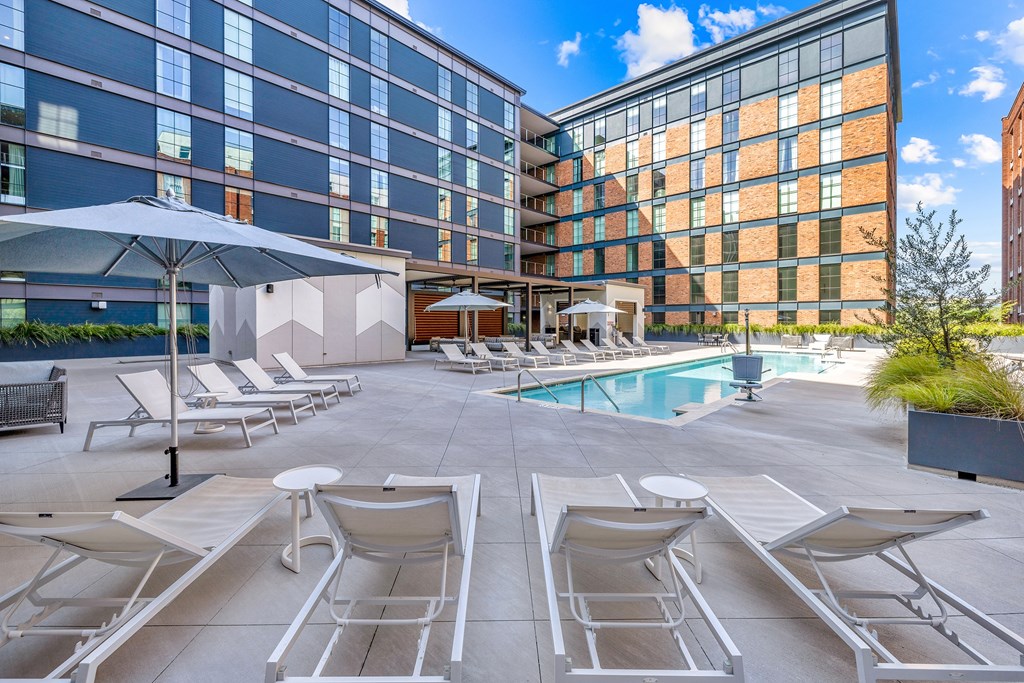 A pool area with sun loungers and umbrellas in front of a modern building.