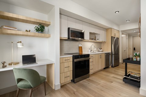 A modern kitchen with a green chair and a laptop on the desk.