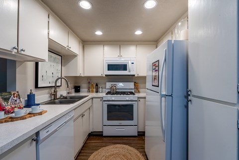A kitchen with white cabinets and appliances, a blue refrigerator, and a stove top oven.