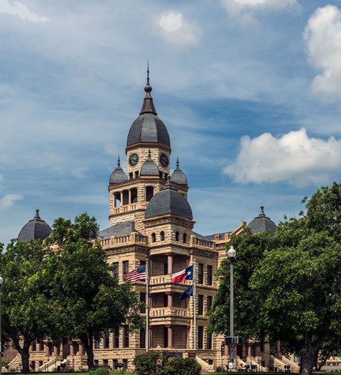 A large, ornate building with a clock tower is surrounded by trees.