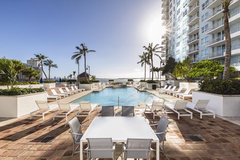 A pool area with chairs and a table with a view of the beach.