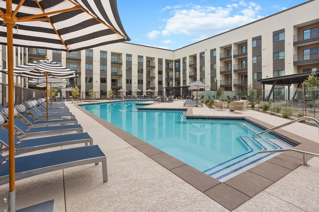 A large swimming pool is surrounded by sun loungers and umbrellas.