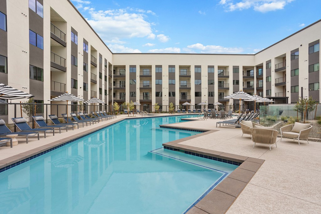A large swimming pool in front of a building with sun loungers and umbrellas.