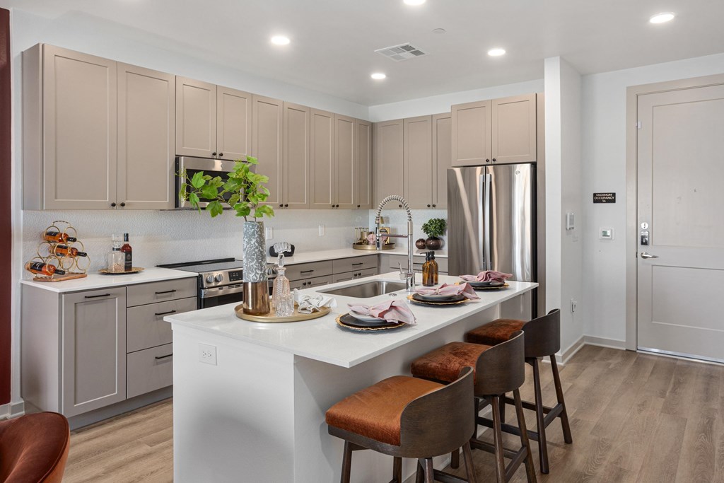 A modern kitchen with a white island and brown chairs.