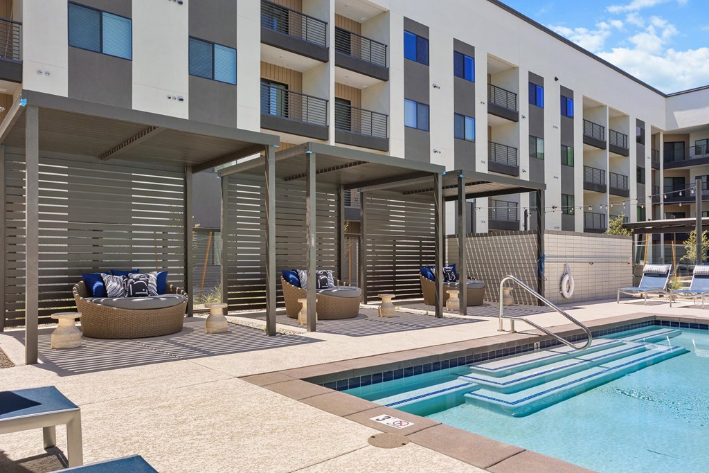 A swimming pool is surrounded by sun loungers and a building with balconies.