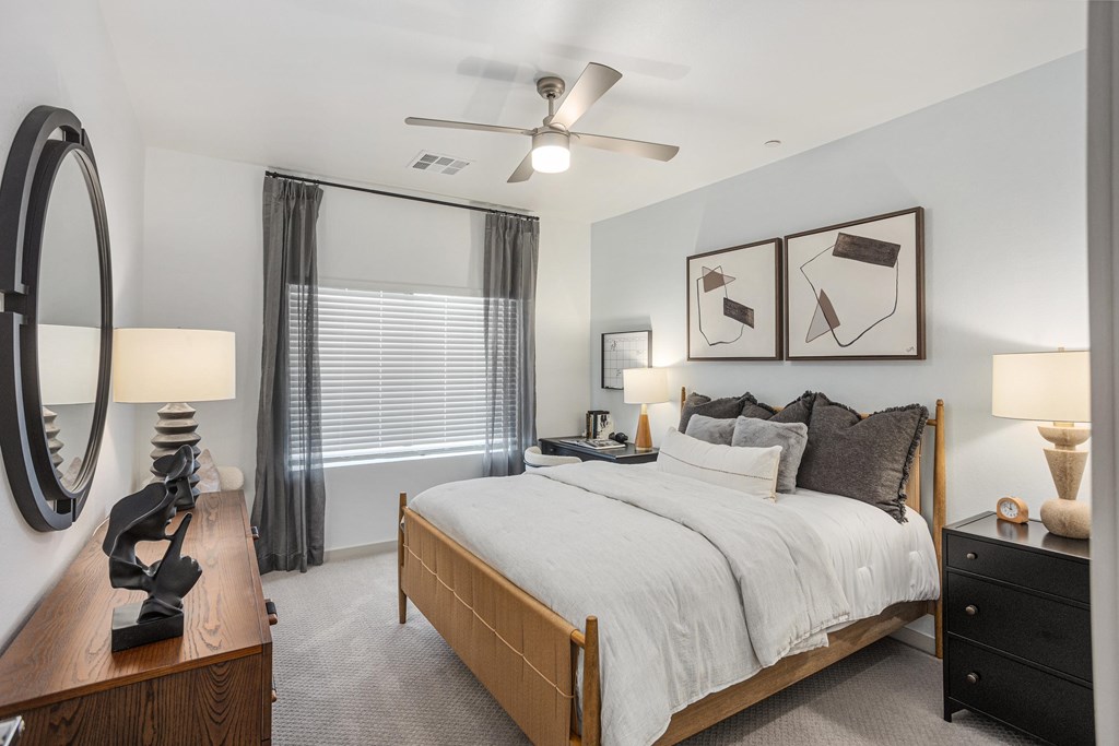 A bedroom with a large bed, a ceiling fan, and a nightstand with a lamp.