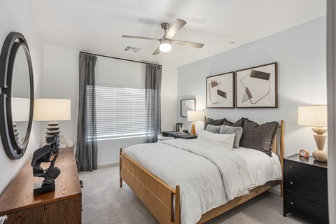 A bedroom with a large bed, a ceiling fan, and a nightstand with a lamp.