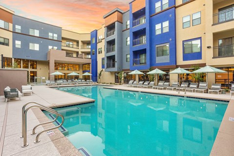 A swimming pool surrounded by apartment buildings and lounge chairs.