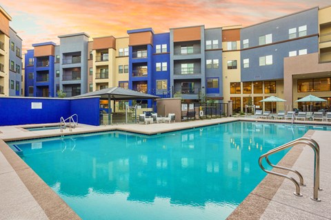 A swimming pool in front of a building with a sunset in the background.