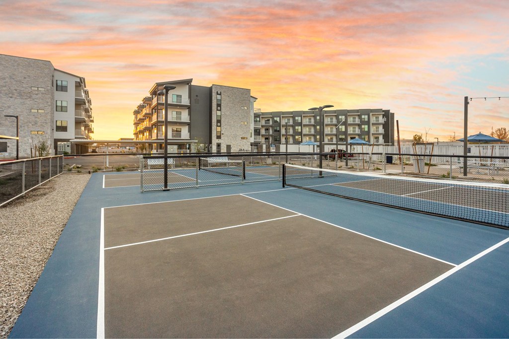A tennis court is surrounded by apartment buildings.