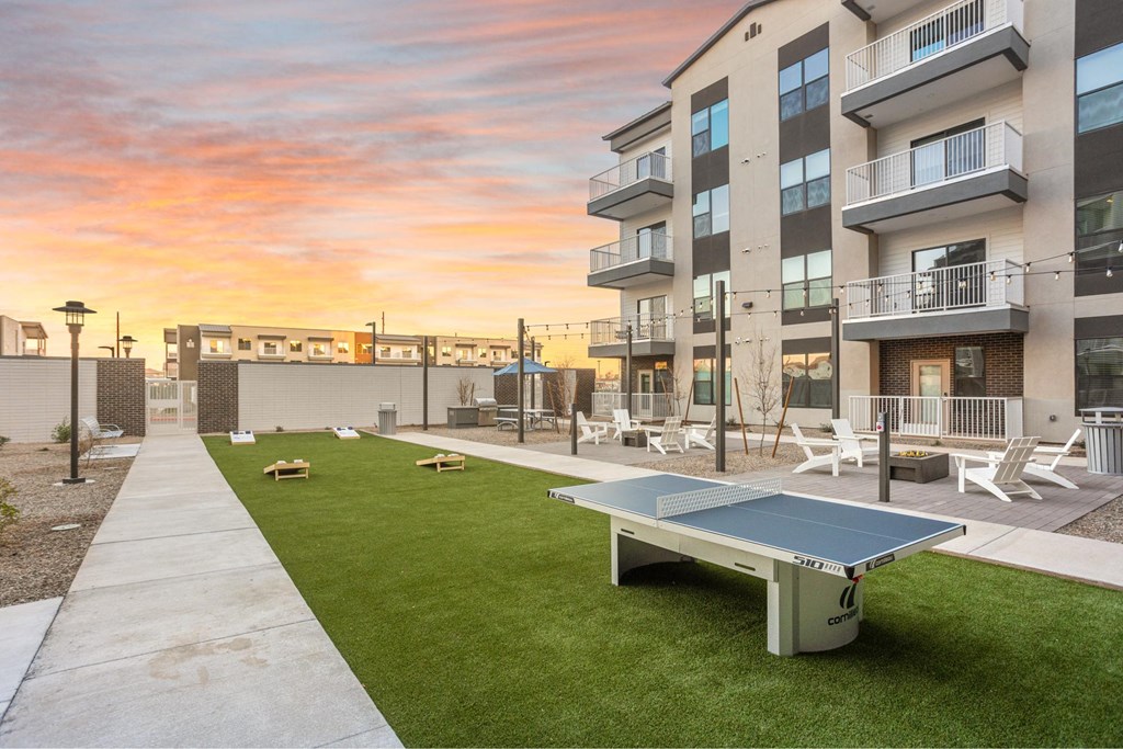 A table tennis table is in the middle of a grassy area in front of apartment buildings.